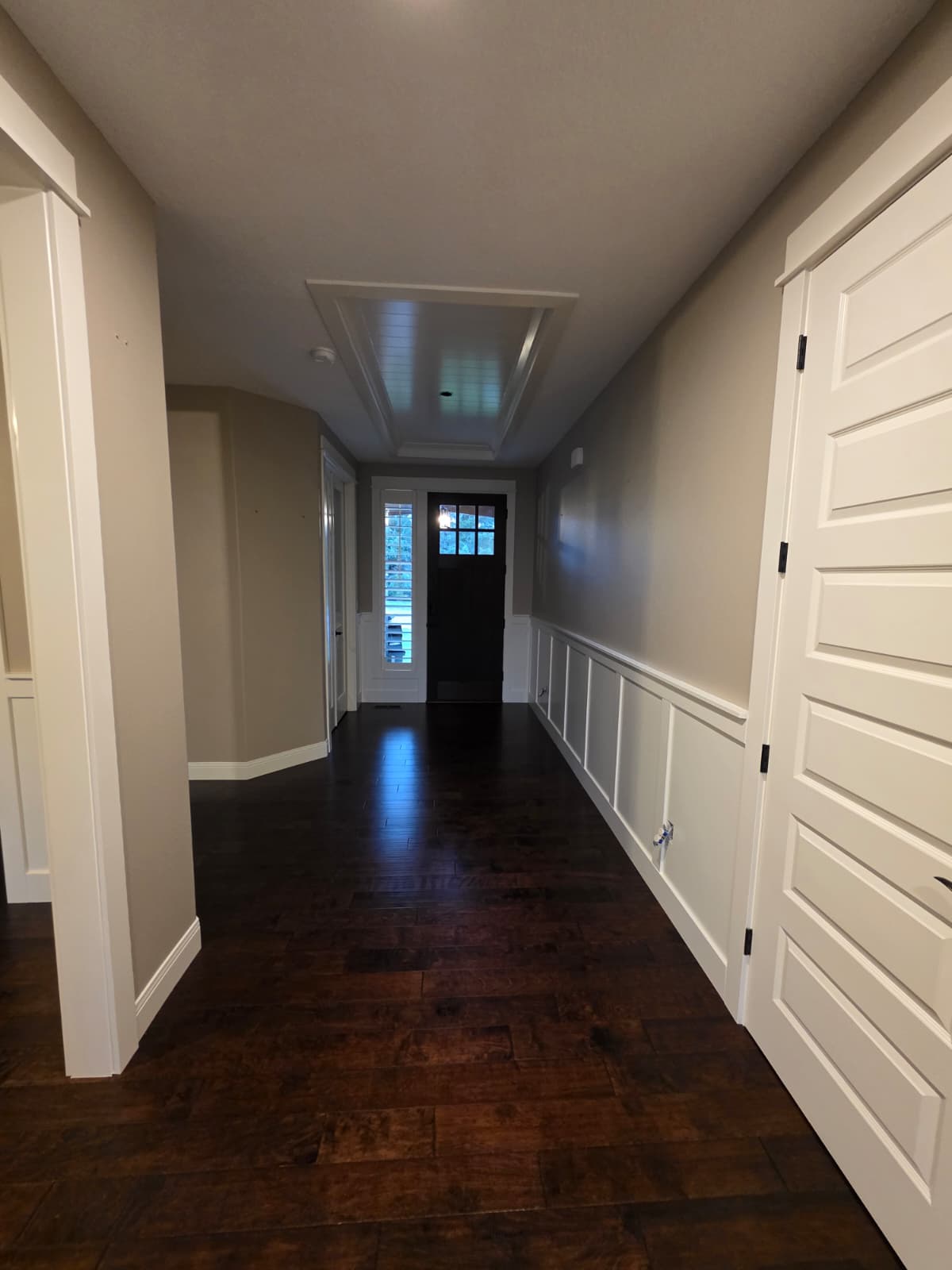 Finished hallway with taupe walls, white wainscoting, and dark hardwood floor