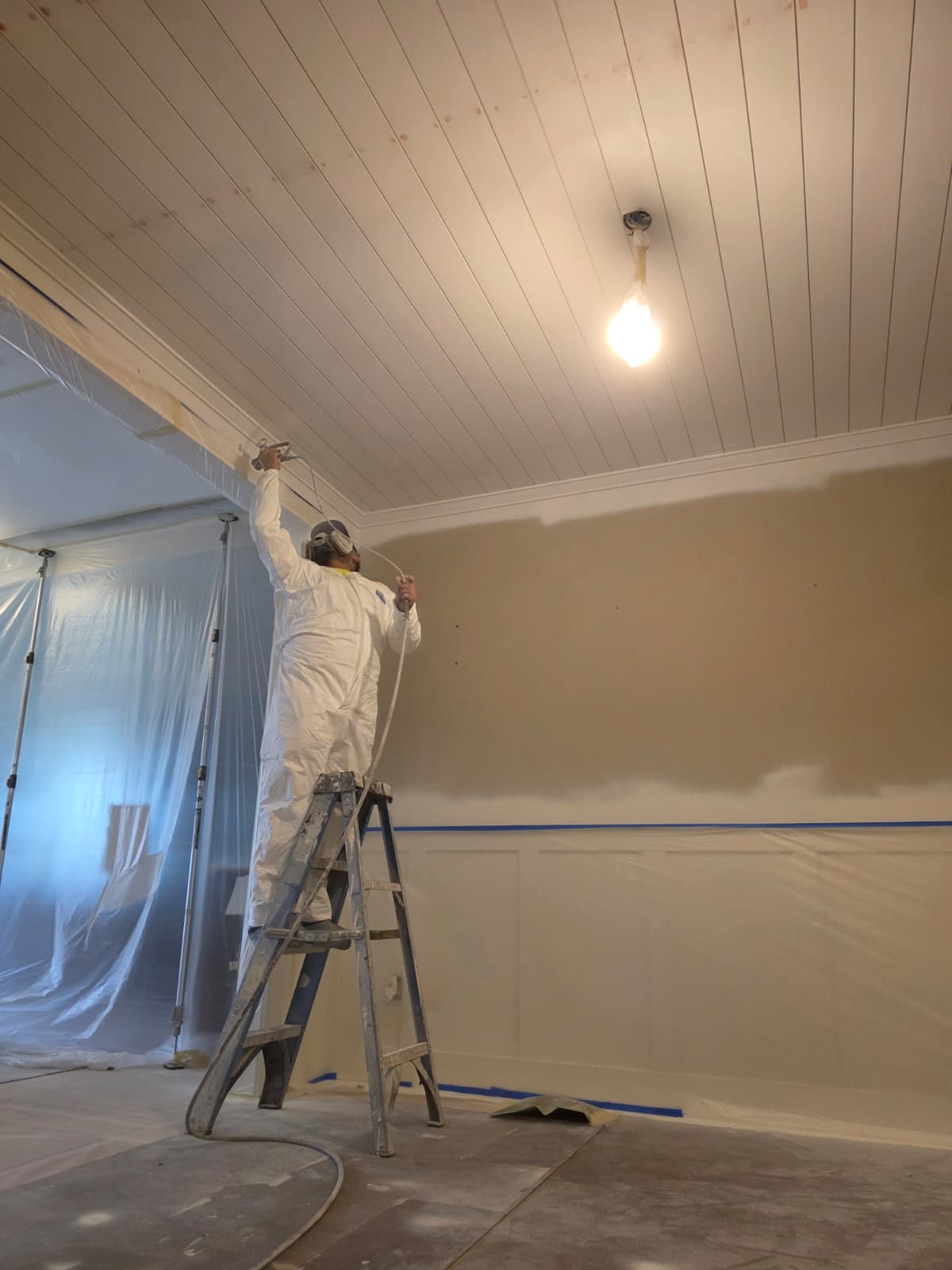 Simply Pro Painting crew member spraying finish on an interior ceiling with the space fully masked
